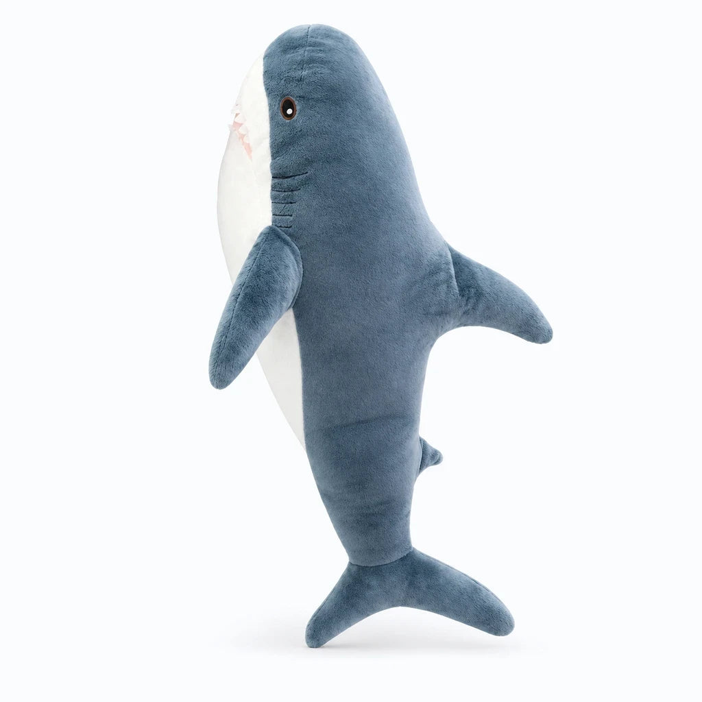 Geante peluche requin disponible en plusieurs largeurs, posée sur un lit